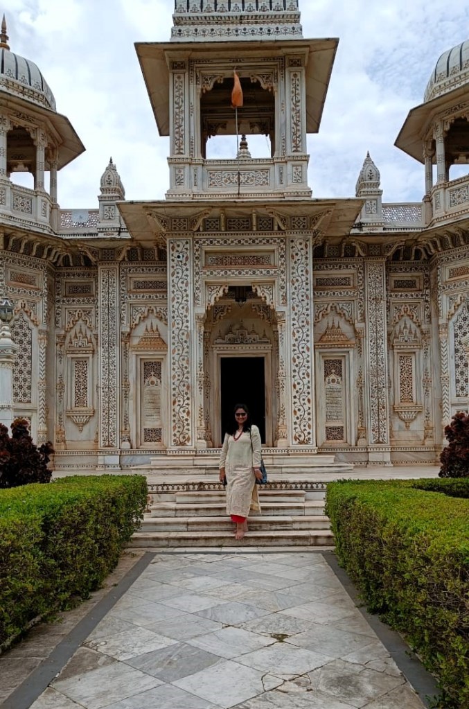 An Indian woman smiles for the camera in front of a marble cenotaph