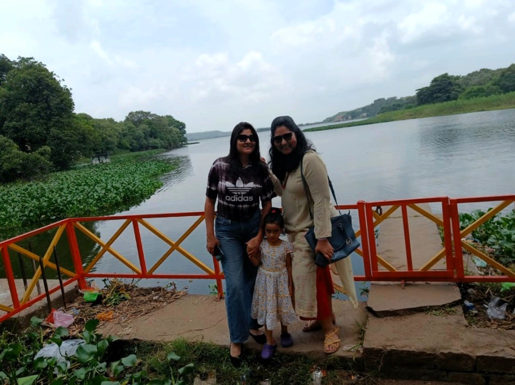 Two Indian women & a girl pose in front of a lake.