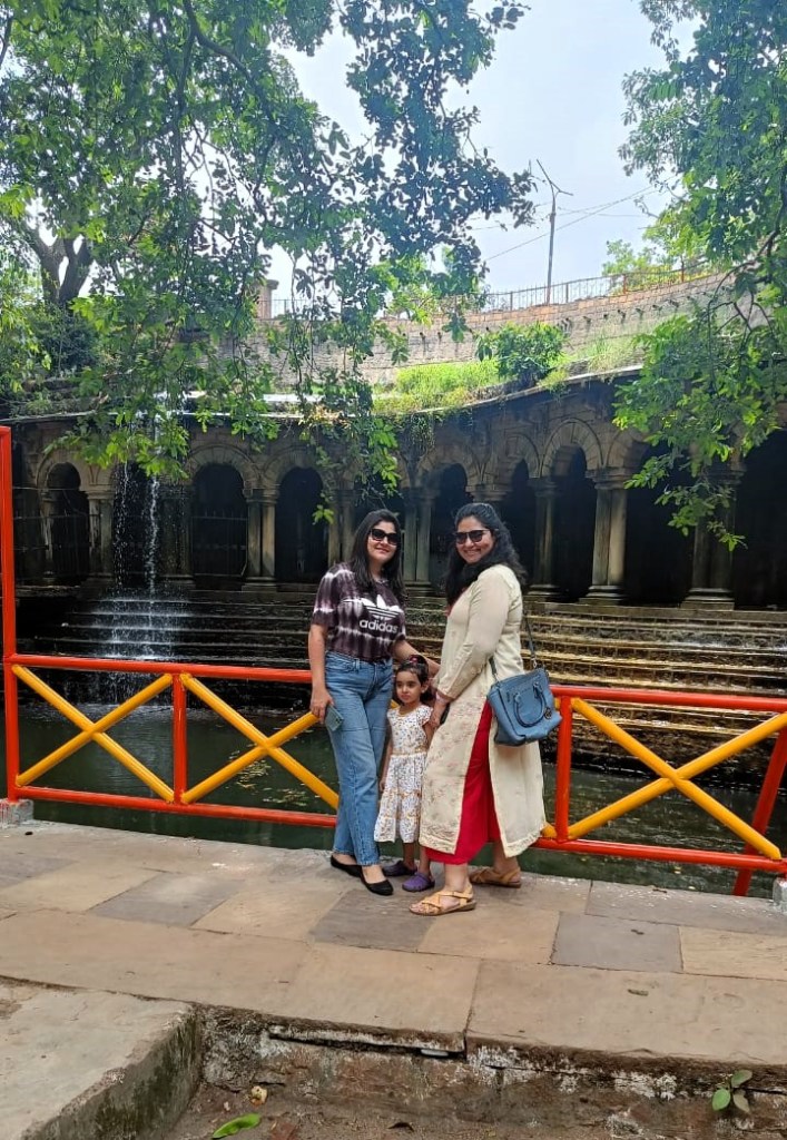Two Indian women & a child smile for the camera in front of a waterfall tank