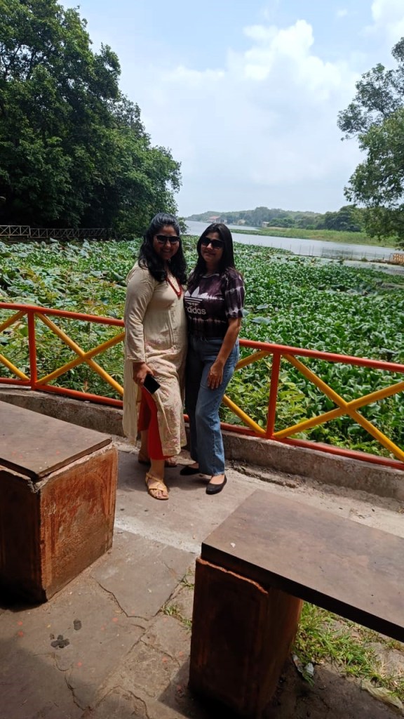 Two Indian women pose in front of a water hyacinth - covered lake.