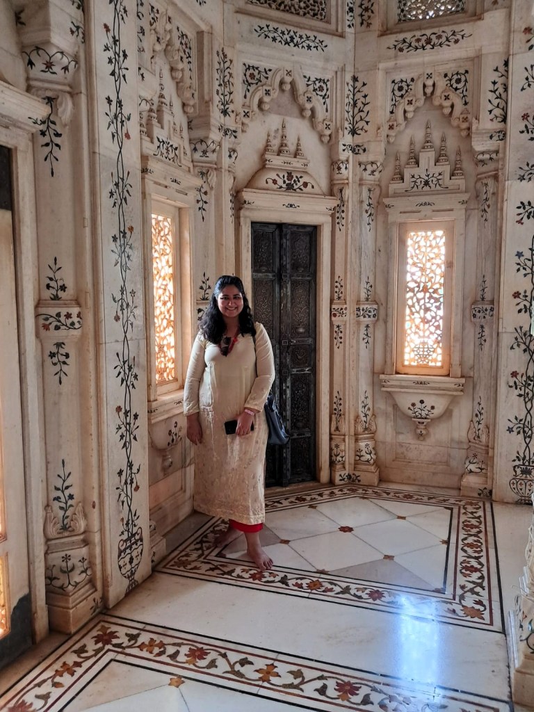 An Indian woman smiles for the camera in front of a silver door.