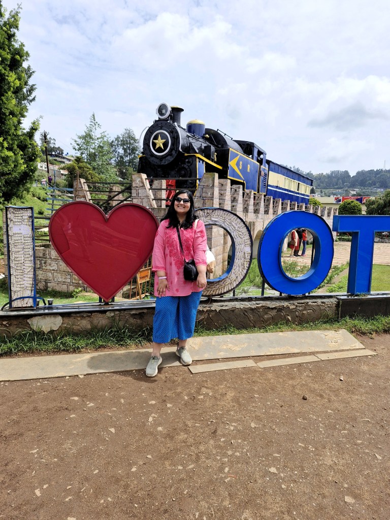 Standing in front of a Nilgiri Mountain Railway engine and a I Love Ooty sign
